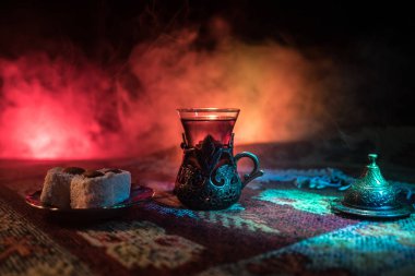 Cam bir halı ile ışık ve duman koyu arka plan üzerinde Doğu snacks ile Arap tea. Doğu çay kavramı. Boş alanı. Seçici odak.