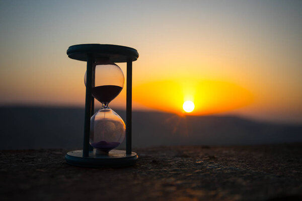 Hourglass Passing of Time Lapse Clouds. An hourglass in front of a bright blue sky with puffy white clouds passing. Time concept. Sunset time. Selective focus