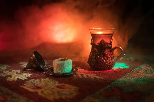 阿拉伯茶在玻璃与东方小吃在地毯上的黑暗背景与灯光和烟雾 东方茶的概念 空的空间 选择性聚焦 — 图库照片