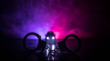 Polis baskını gece ve sen altında tutuklama kavramı vardır. Kelepçe arka polis araba ile silüeti. Görüntü yanıp sönen kırmızı ve mavi polis ışıklardan sisli arka plan ile. Kaymak vurdu