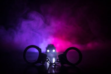 Polis baskını gece ve sen altında tutuklama kavramı vardır. Kelepçe arka polis araba ile silüeti. Görüntü yanıp sönen kırmızı ve mavi polis ışıklardan sisli arka plan ile. Kaymak vurdu