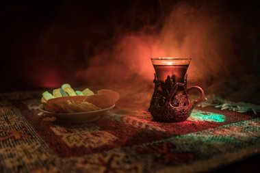 Cam bir halı ile ışık ve duman koyu arka plan üzerinde Doğu snacks ile Arap tea. Doğu çay kavramı. Boş alanı. Seçici odak.