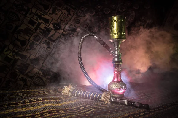 Hookah hot coals on shisha bowl making clouds of steam at Arabian interior. Oriental ornament on the carpet. Stylish oriental shisha in dark with backlight. For Shisha advertisement. Selective focus