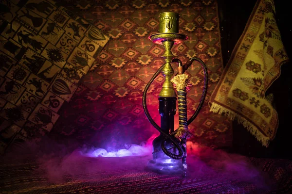 Hookah hot coals on shisha bowl making clouds of steam at Arabian interior. Oriental ornament on the carpet. Stylish oriental shisha in dark with backlight. For Shisha advertisement. Selective focus