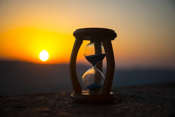 Hourglass Passing of Time Lapse Clouds. An hourglass in front of a bright blue sky with puffy white clouds passing. Time concept. Sunset time. Selective focus