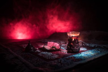 Cam bir halı ile ışık ve duman koyu arka plan üzerinde Doğu snacks ile Arap tea. Doğu çay kavramı. Boş alanı. Seçici odak.