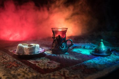 Cam bir halı ile ışık ve duman koyu arka plan üzerinde Doğu snacks ile Arap tea. Doğu çay kavramı. Boş alanı. Seçici odak.