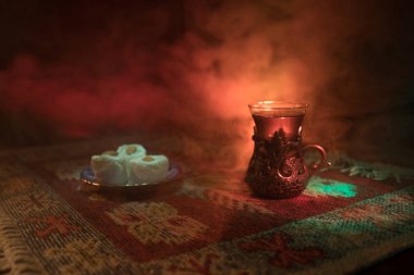 Cam bir halı ile ışık ve duman koyu arka plan üzerinde Doğu snacks ile Arap tea. Doğu çay kavramı. Boş alanı. Seçici odak.