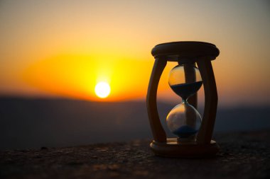 Kum saati geçen zaman atlamalı bulutlar. Bir kum saati önünde parlak mavi gökyüzü ile kabarık beyaz bulutlar geçiyor. Zaman kavramı. Günbatımı zamanı. Seçici odak