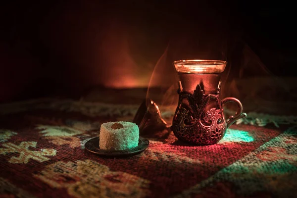 Cam bir halı ile ışık ve duman koyu arka plan üzerinde Doğu snacks ile Arap tea. Doğu çay kavramı. Boş alanı. Seçici odak.