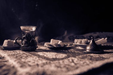 Cam bir halı ile ışık ve duman koyu arka plan üzerinde Doğu snacks ile Arap tea. Doğu çay kavramı. Boş alanı. Seçici odak.