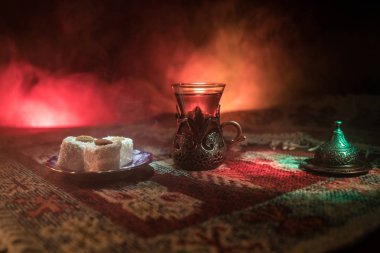 Cam bir halı ile ışık ve duman koyu arka plan üzerinde Doğu snacks ile Arap tea. Doğu çay kavramı. Boş alanı. Seçici odak.