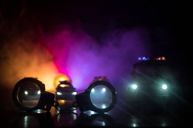 Polis baskını gece ve sen altında tutuklama kavramı vardır. Kelepçe arka polis araba ile silüeti. Görüntü yanıp sönen kırmızı ve mavi polis ışıklardan sisli arka plan ile. Kaymak vurdu