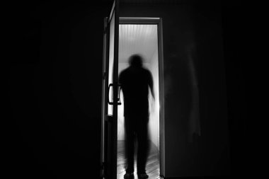 Kapalı cam bir kapıdan geçen, bilinmeyen bir gölge figürünün silueti. Geceleri pencerenin önündeki bir insanın silueti. Manyağın bulanık silueti korkunç cadılar bayramı konsepti.