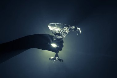 Martini kokteyl cam el koyu tonda dumanlı arka plan veya renkli kokteyl cam su sıçramalarına ve zeytin sıçramasına. Parti club eğlence. Karışık ışık. Seçici odak