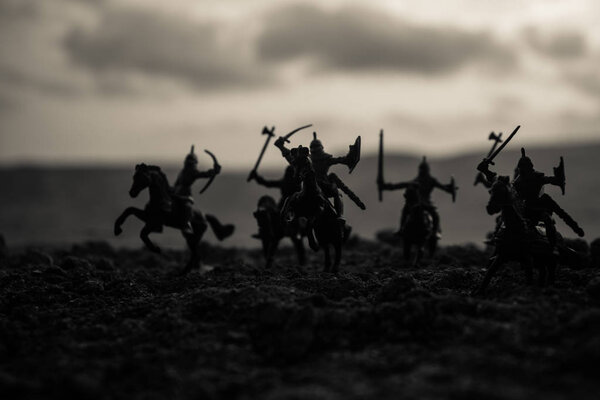 Medieval battle scene with cavalry and infantry. Silhouettes of figures as separate objects, fight between warriors on sunset foggy background. Selective focus
