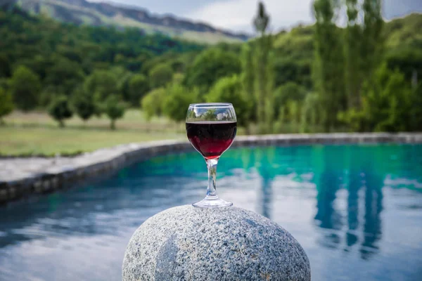 Drink in tall glass in poolside. Refreshment on summer day. Purple juice cocktail or vine. Mountain forest background. Selective focus