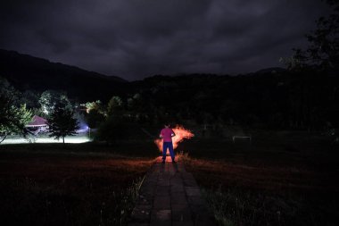 Adam gece ormanda silüeti. Işık ile karanlık ormanın içinde duran kişi silüeti. Karanlık gece ormanda. Gerçeküstü gece orman sahne. Korku Cadılar Bayramı kavramı.
