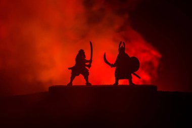 Düelloda iki Ortaçağ savaşçıları silüeti. Karanlık kılıçla ile iki savaşçı resimle sisli arka plan tonda. Seçici odak.