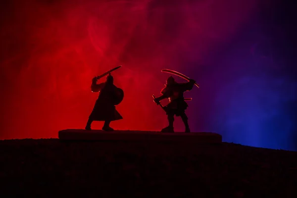 Silhouette of two medieval warriors in duel. Picture with two fighter with sword with dark toned foggy background. Selective focus.
