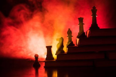 Business hierarchy. Strategy concept with chess pieces. Chess standing on a pyramid of books with the king at the top. Dark foggy background with toned light. Copy space. clipart