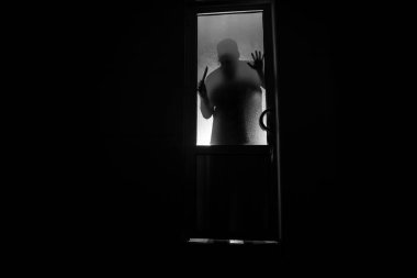 Kapalı cam bir kapıdan geçen, bilinmeyen bir gölge figürünün silueti. Geceleri pencerenin önündeki bir insanın silueti. Manyağın bulanık silueti korkunç cadılar bayramı konsepti.