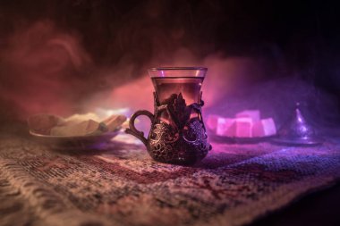 Cam bir halı ile ışık ve duman koyu arka plan üzerinde Doğu snacks ile Arap tea. Doğu çay kavramı. Boş alanı. Seçici odak.