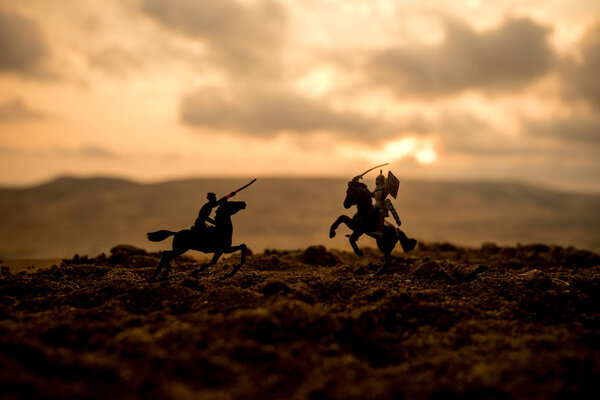 Средневековая боевая сцена с кавалерией и пехотой. Силуэты фигур как отдельные объекты, борьба между воинами на закатном туманном фоне. Селективный фокус
