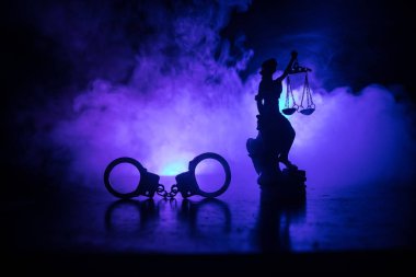 Legal law concept. Silhouette of handcuffs with The Statue of Justice on backside with the flashing red and blue police lights at foggy background. Selective focus clipart