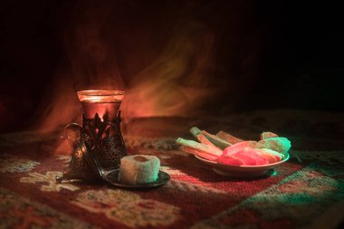 Cam bir halı ile ışık ve duman koyu arka plan üzerinde Doğu snacks ile Arap tea. Doğu çay kavramı. Boş alanı. Seçici odak.