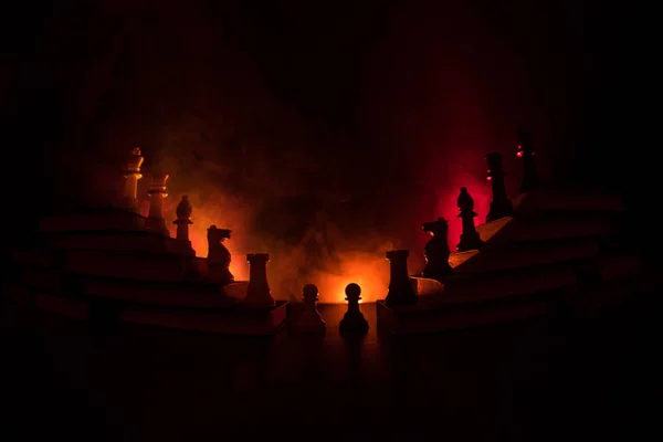 Business hierarchy. Strategy concept with chess pieces. Chess standing on a pyramid of books with the king at the top. Dark foggy background with toned light. Copy space.