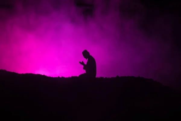 Silhouette of praying Muslim man on toned foggy background. Ramadan Kareem background. Muslim Eid holiday decoration. Praying people religion concept. Selective focus