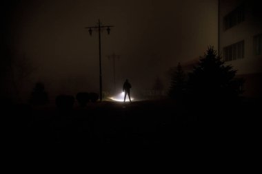 Gece manzarası. Gece yoğun sis içinde şehir. Mistik manzara ürkütücü adam gerçeküstü ışıklarla. Yapay ışıkta gece siste yürüyen adamın siluet. Arka aydınlatma karışık güzel.