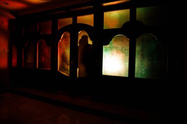 Kapalı cam bir kapıdan geçen, bilinmeyen bir gölge figürünün silueti. Geceleri pencerenin önündeki bir insanın silueti. Manyağın bulanık silueti korkunç cadılar bayramı konsepti.