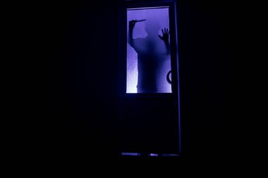 Kapalı cam bir kapıdan geçen, bilinmeyen bir gölge figürünün silueti. Geceleri pencerenin önündeki bir insanın silueti. Manyağın bulanık silueti korkunç cadılar bayramı konsepti.