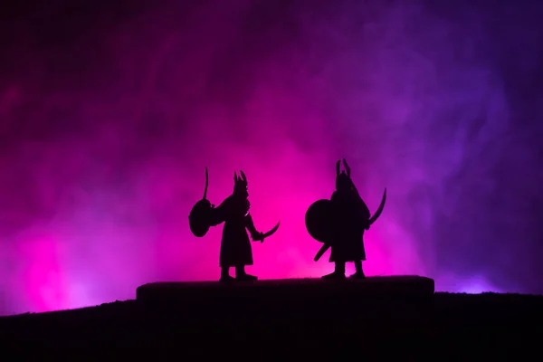 Silhouette of two medieval warriors in duel. Picture with two fighter with sword with dark toned foggy background. Selective focus.