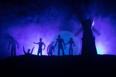 Aç zombiler ve karanlık sisli tonda gökyüzü karşı tepede eski fırıldak siluetleri kalabalık. Siluetleri korkunç zombi gece yürüyüş. Korku kavramı