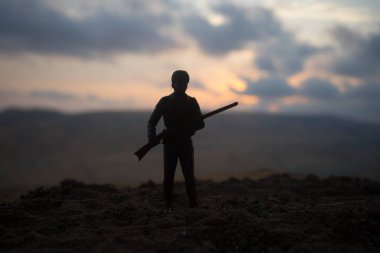 Askeri asker veya memur batımında silahlarla silüeti. atış, elinde silah, renkli gökyüzü, dağ, arka plan. Oyuncak asker ile dekorasyon