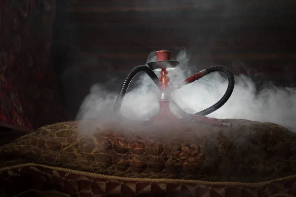 Hookah hot coals on shisha bowl making clouds of steam at Arabian interior. Oriental ornament on the carpet. Stylish oriental shisha with backlight. For Shisha advertisement. Selective focus