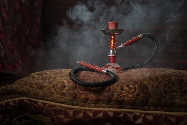 Hookah hot coals on shisha bowl making clouds of steam at Arabian interior. Oriental ornament on the carpet. Stylish oriental shisha with backlight. For Shisha advertisement. Selective focus