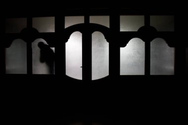 Kapalı cam bir kapıdan geçen, bilinmeyen bir gölge figürünün silueti. Geceleri pencerenin önündeki bir insanın silueti. Manyağın bulanık silueti korkunç cadılar bayramı konsepti.