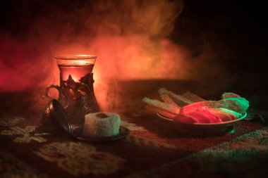 Cam bir halı ile ışık ve duman koyu arka plan üzerinde Doğu snacks ile Arap tea. Doğu çay kavramı. Boş alanı. Seçici odak.