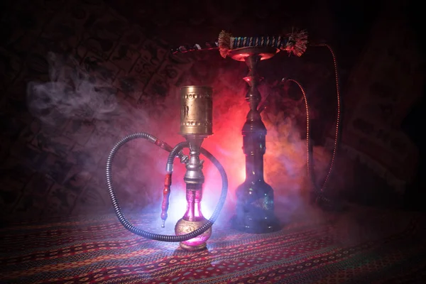 Hookah hot coals on shisha bowl making clouds of steam at Arabian interior. Oriental ornament on the carpet. Stylish oriental shisha in dark with backlight. For Shisha advertisement. Selective focus