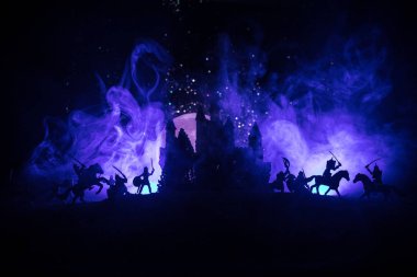 Süvari ve piyadelerle ortaçağ savaş sahnesi. Şekillerin siluetleri ayrı nesneler olarak, karanlık tonlu sisli arka planda ortaçağ şatosuyla savaşan savaşçılar arasında. Seçici odak