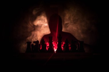 Adam satranç oynamaktan. Satranç satranç figürleri ile bir kişi korkunç bulanık silüeti. Sisli arka plan koyu tonda. Seçici odak. Korku kavramı