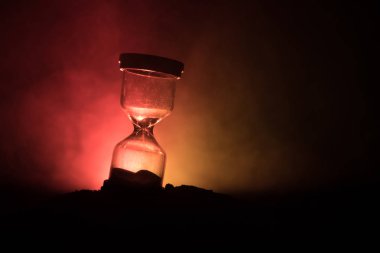 Time concept. Silhouette of Hourglass clock and smoke on dark background with hot yellow orange red blue cold back lighting, with copy space. Selective focus clipart