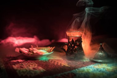 Cam bir halı ile ışık ve duman koyu arka plan üzerinde Doğu snacks ile Arap tea. Doğu çay kavramı. Boş alanı. Seçici odak.