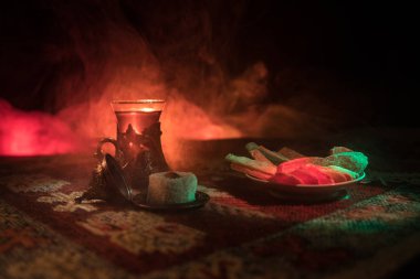 Cam bir halı ile ışık ve duman koyu arka plan üzerinde Doğu snacks ile Arap tea. Doğu çay kavramı. Boş alanı. Seçici odak.