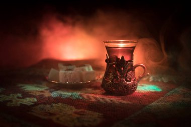 Cam bir halı ile ışık ve duman koyu arka plan üzerinde Doğu snacks ile Arap tea. Doğu çay kavramı. Boş alanı. Seçici odak.