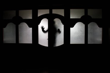 Kapalı cam bir kapıdan geçen, bilinmeyen bir gölge figürünün silueti. Geceleri pencerenin önündeki bir insanın silueti. Manyağın bulanık silueti korkunç cadılar bayramı konsepti.